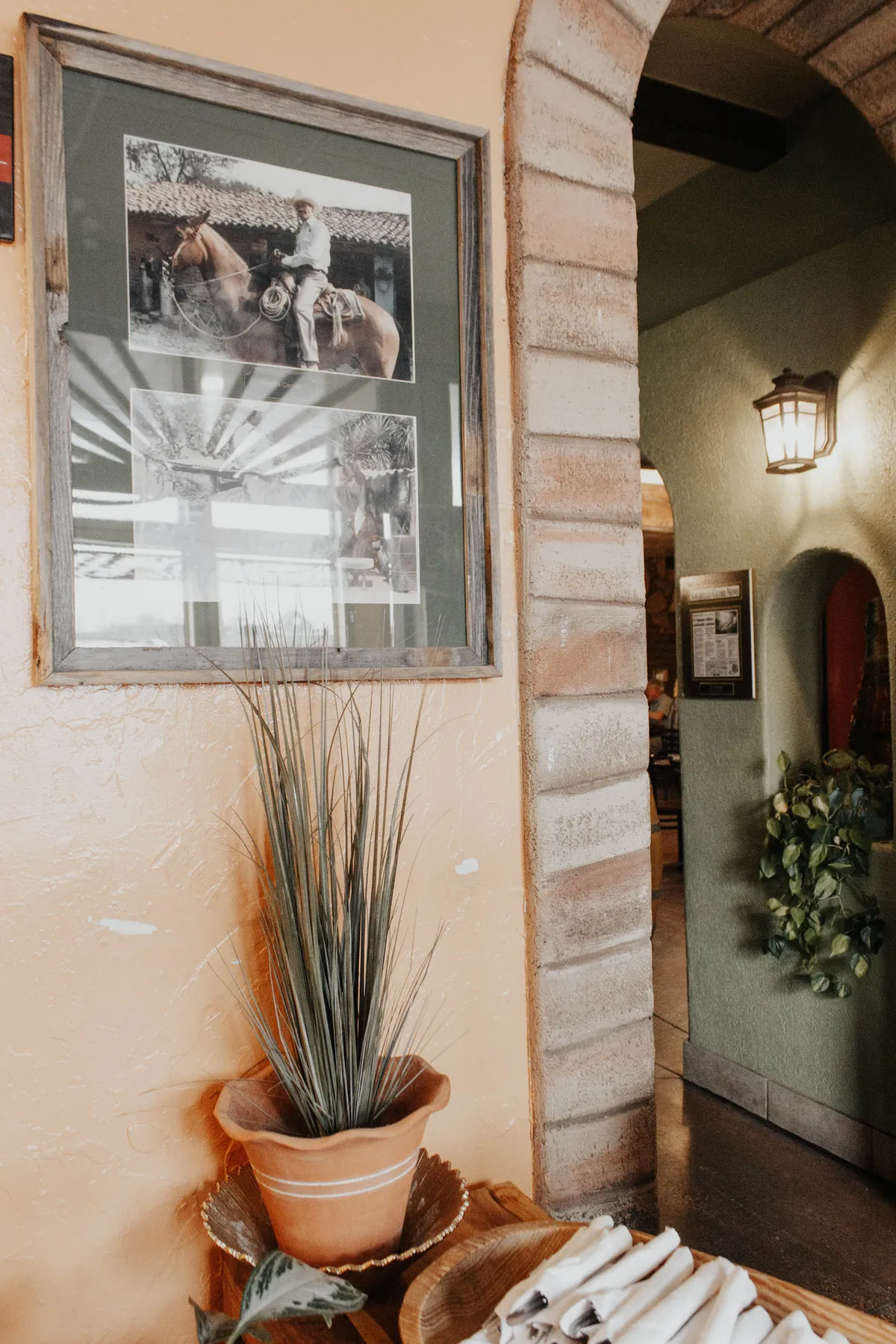 El Tejavan dining room: orange stucco wall, a framed photograph of a rider on horseback, a stone archway and a wrought-iron lantern
