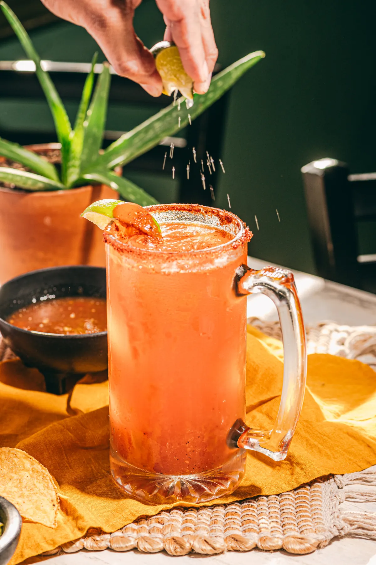 A michelada in a handled glass mug with a chili-salt rim and lime