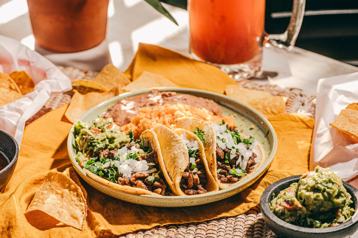 A plate of street tacos with rice, beans and guacamole in afternoon sun