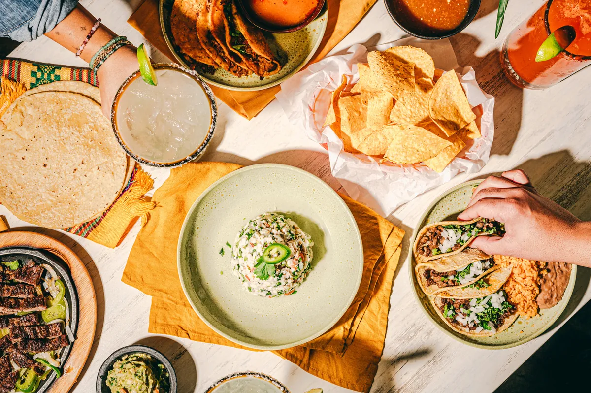 Overhead view of a shared table: fajitas, tacos, ceviche, chips and salsa, guacamole and margaritas